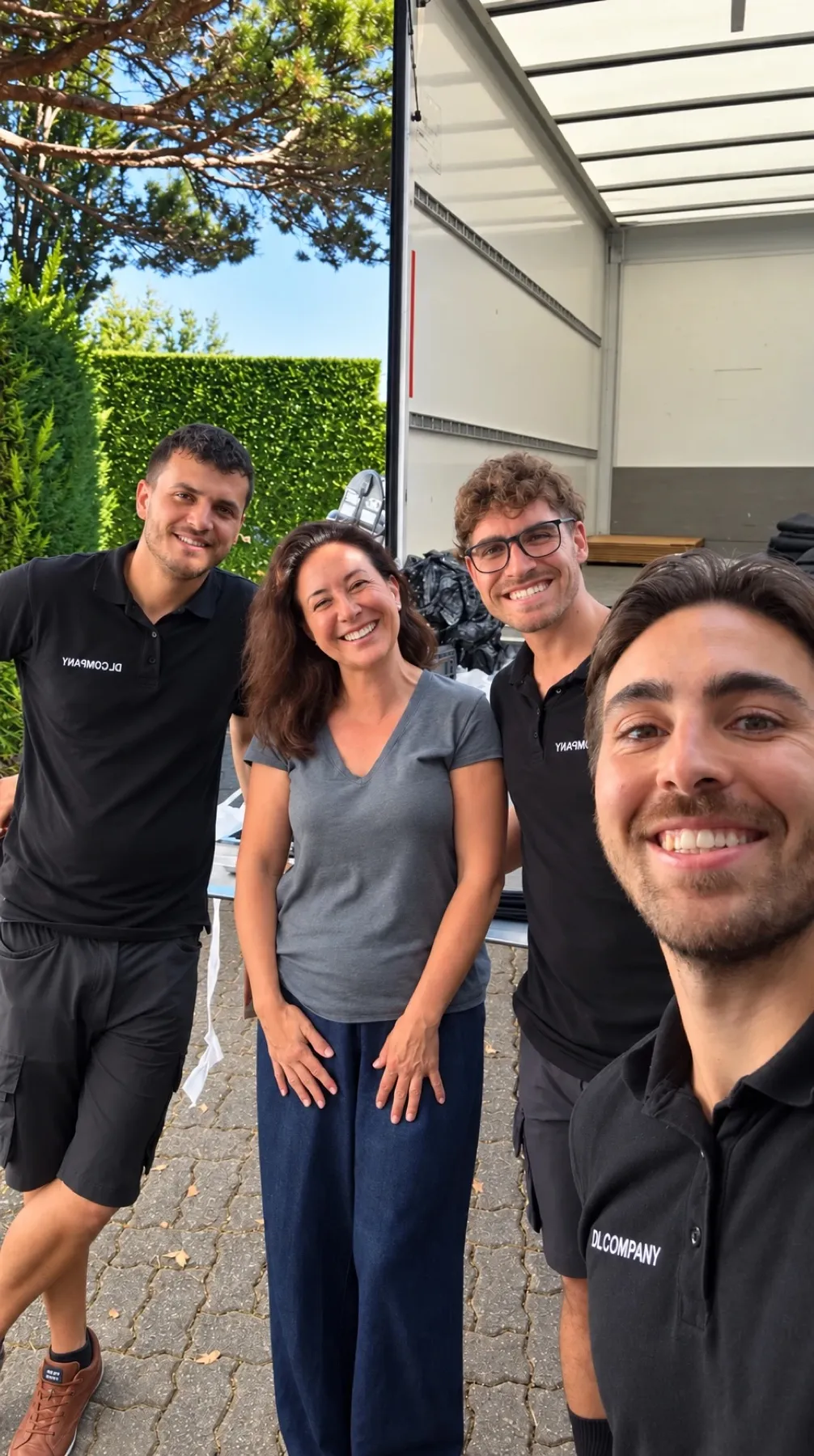 Isabelle souriante entre trois déménageurs DL Company devant le camion ouvert, le jour du déménagement